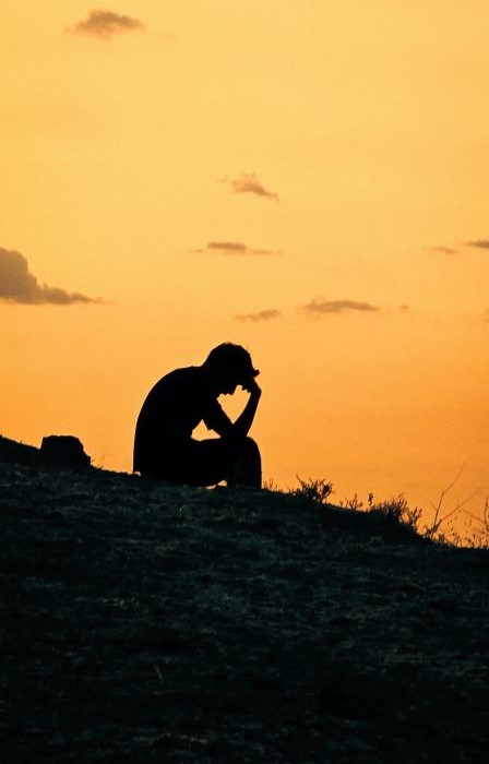 Silhouette of man sitting on hillside with head in hands